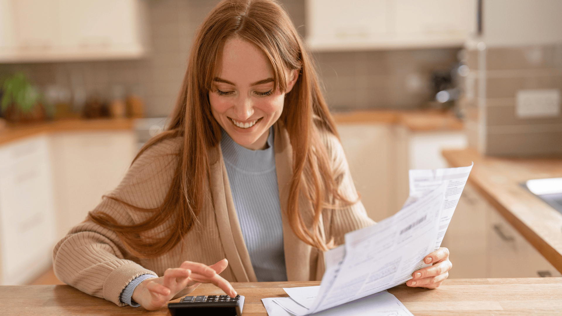 Mujer joven usando una calculadora mientras revisa unas facturas en la cocina