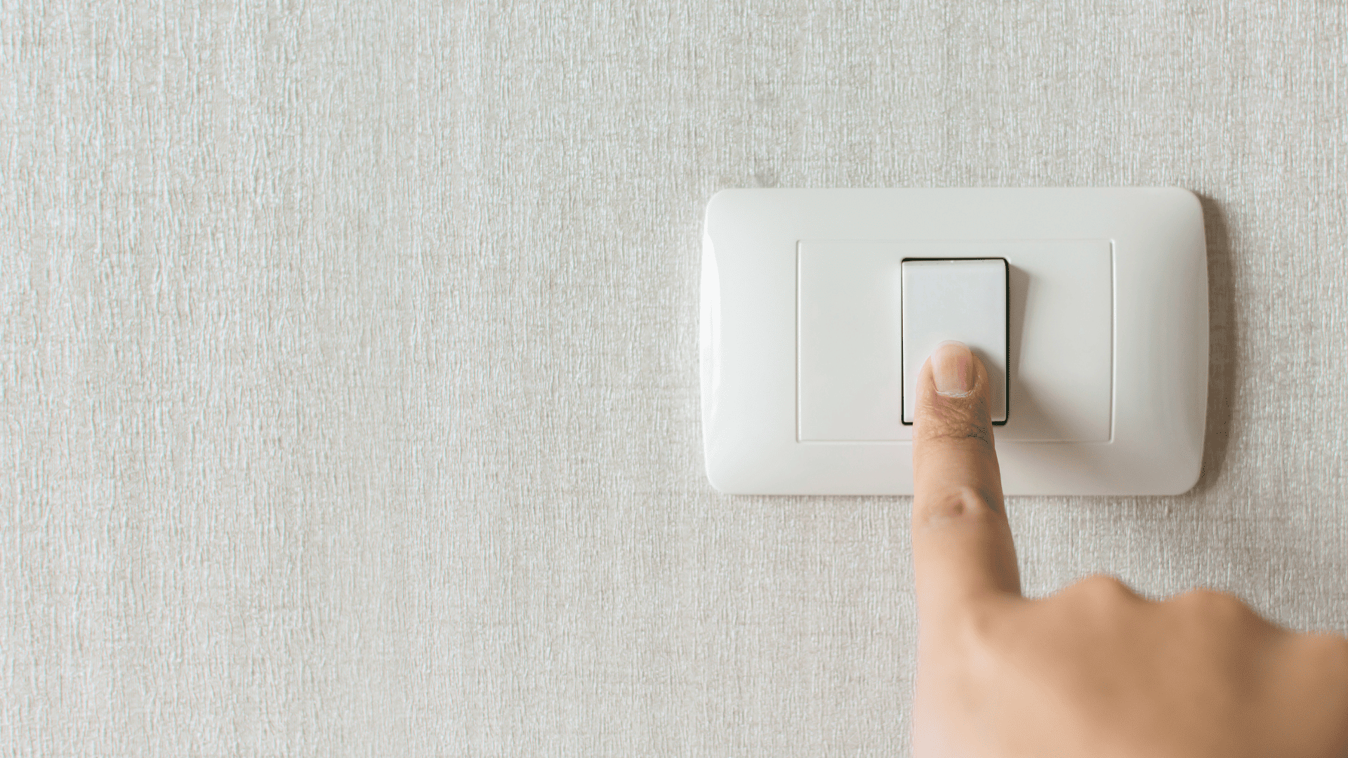 Imagen de un dedo presionando un interruptor de luz en una pared con textura clara, ilustrando el acto de encender o apagar la electricidad.