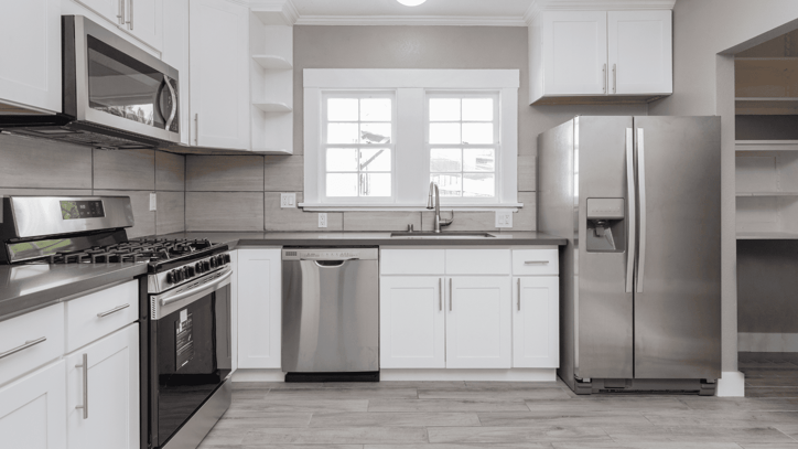 Cocina moderna con electrodomésticos de acero inoxidable, incluyendo frigorífico, lavavajillas, horno y microondas, todo en un entorno de diseño limpio y minimalista.