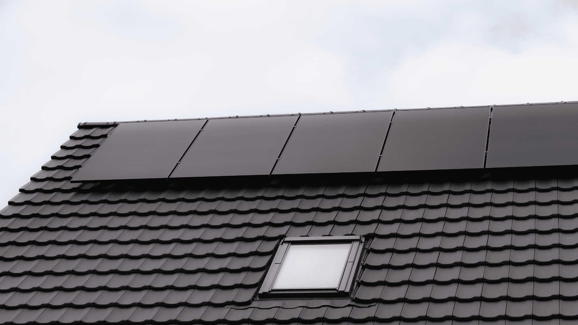 Paneles solares negros instalados sobre un tejado oscuro con ventana.