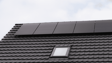 Paneles solares negros instalados sobre un tejado oscuro con ventana.