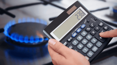 Mano usando una calculadora frente a una cocina de gas encendida