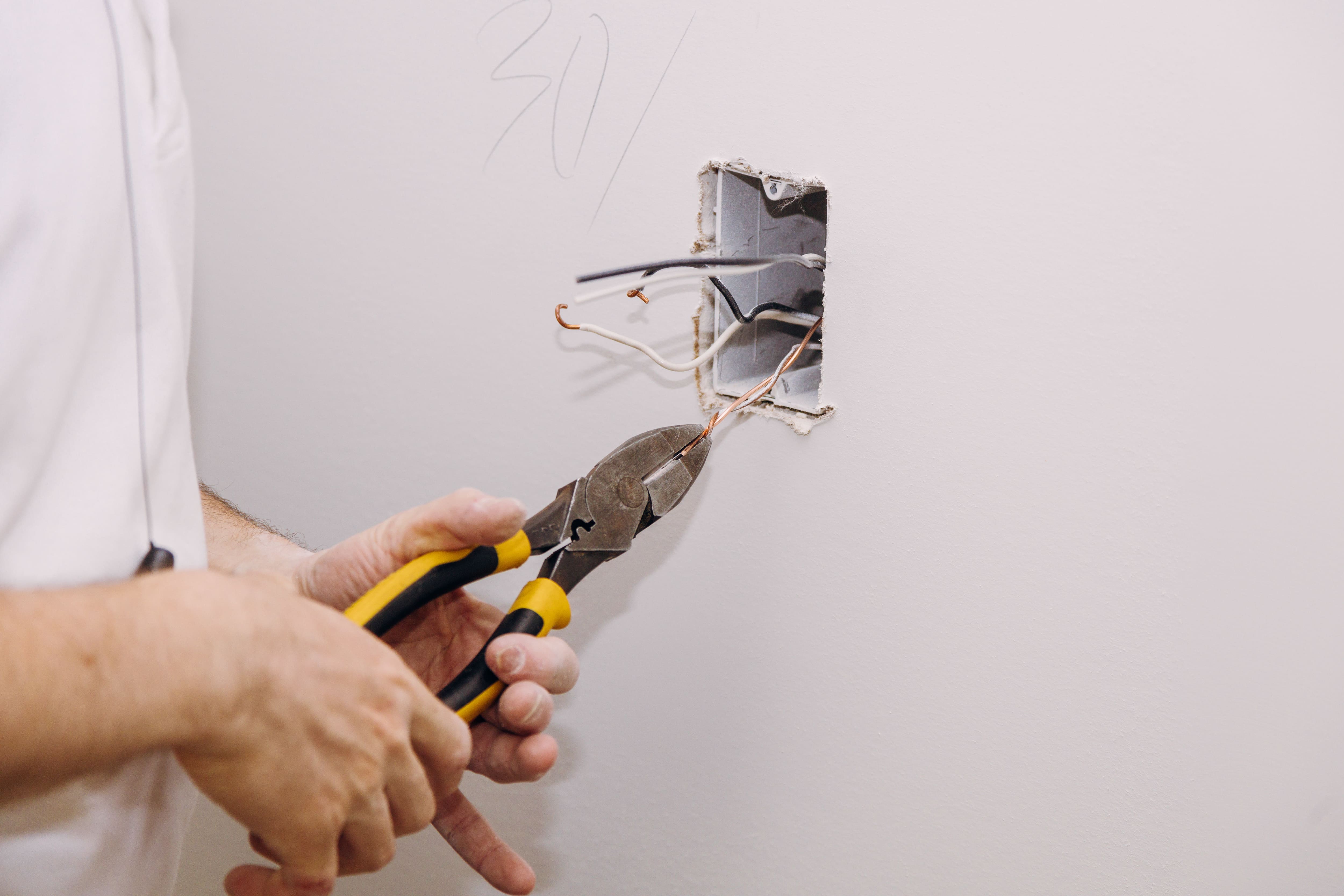 Persona usando alicates para reparar cables eléctricos en una pared