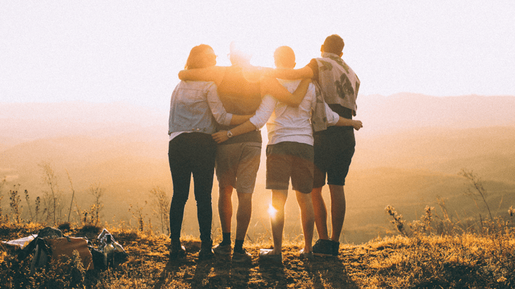 Grupo de amigos abrazados contemplando el atardecer desde una colina