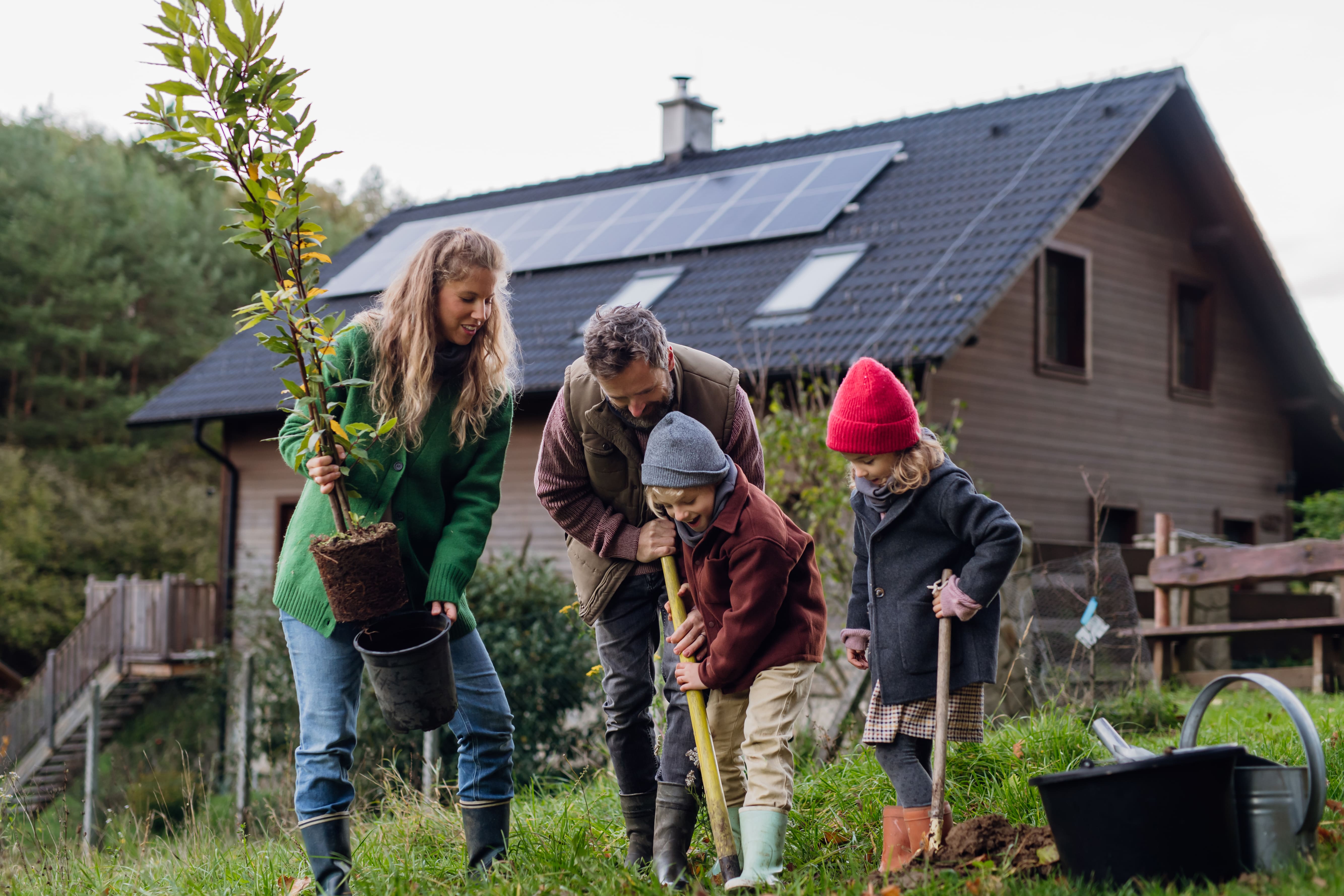 Familia plantando un árbol frente a su casa con placas solares