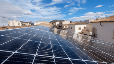 Paneles solares instalados sobre un tejado con vistas a un núcleo urbano y montañas al fondo.