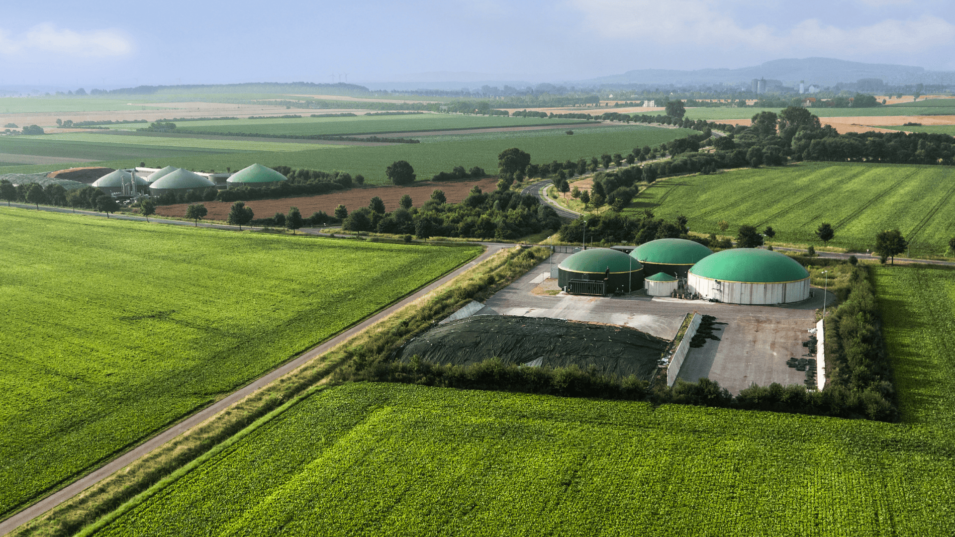 Planta de biogás en entorno rural rodeada de campos agrícolas, ejemplo de generación de energía renovable en el sector agrario.