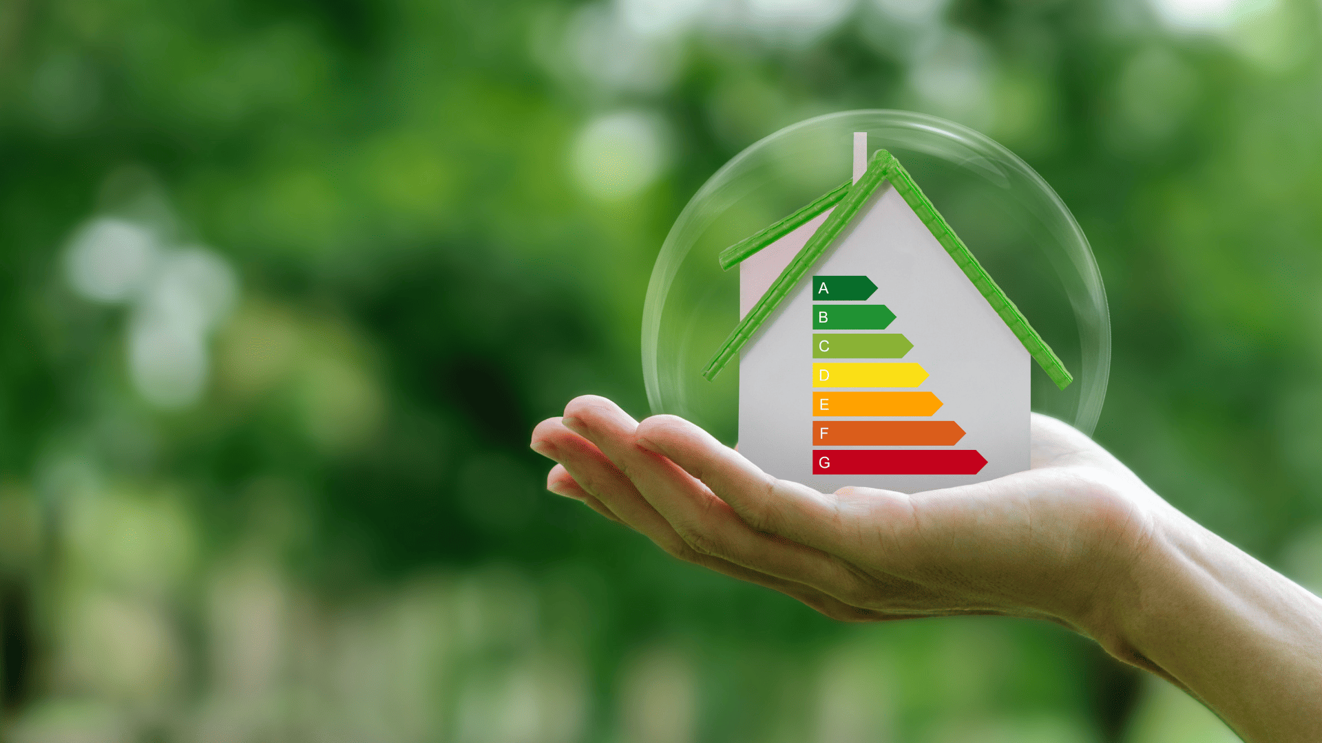 Casa con etiqueta de eficiencia energética sostenida en una mano sobre fondo natural.