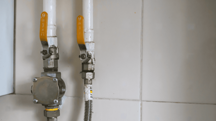Llaves de paso y conexiones de una instalación de gas en una pared alicatada.