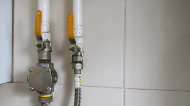 Llaves de paso y conexiones de una instalación de gas en una pared alicatada.