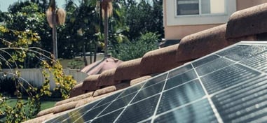 Paneles solares instalados sobre tejado de tejas en zona residencial con palmeras.