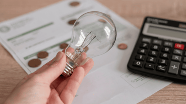 Mano sosteniendo una bombilla con una factura de la luz, monedas y calculadora de fondo