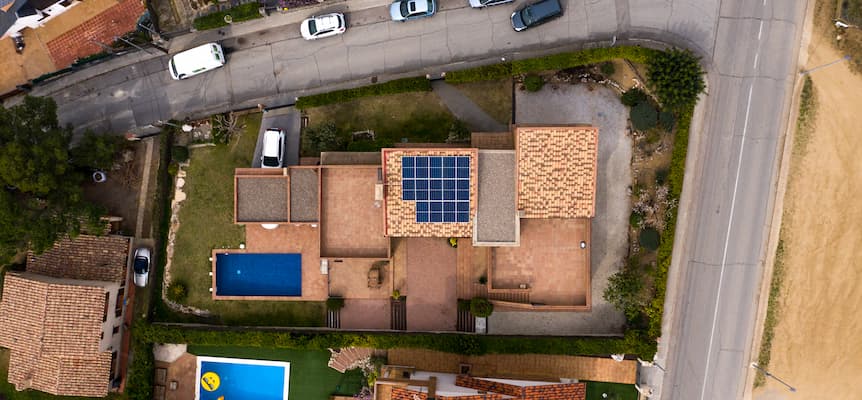Vista aérea captada por un dron de un terreno entre dos carreteras, con una casa en el centro que tiene piscina y placas solares en el tejado
