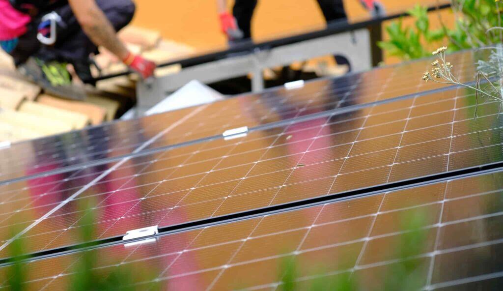 Placa solar en primer plano con dos instaladores trabajando en el fondo