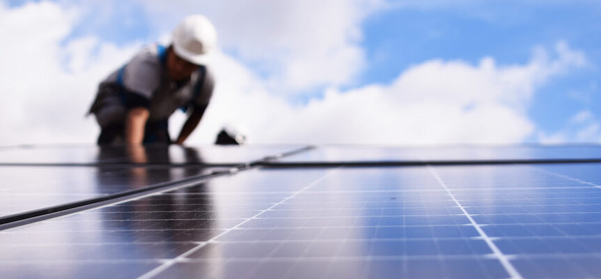 Placa solar en primer plano con un instalador trabajando en el fondo