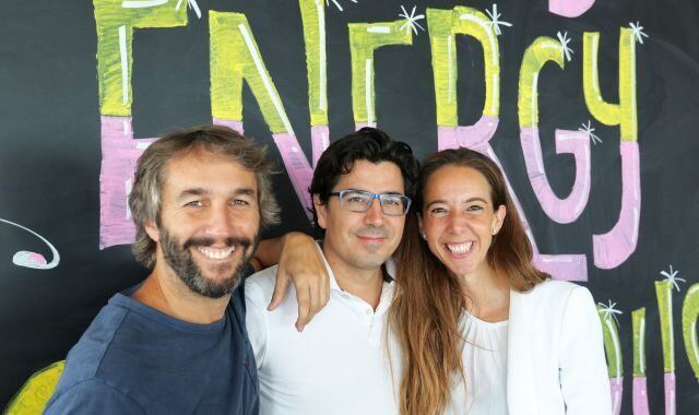 Tres personas sonriendo frente a una pizarra con la palabra "ENERGY" escrita en grande