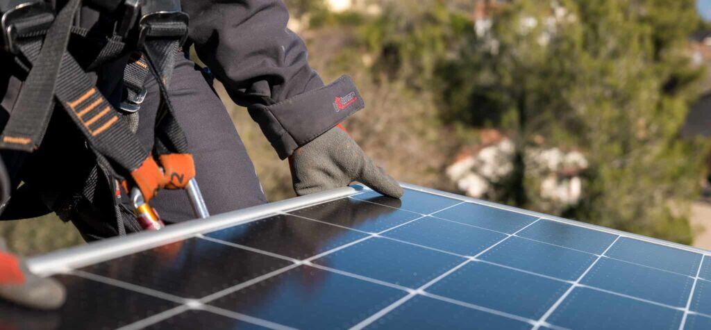 Trabajador con guantes realizando mantenimiento en un panel solar instalado en un tejado