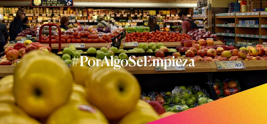 Supermercado con personas comprando en la sección de frutas, con el texto '#PorAlgoSeEmpieza' superpuesto