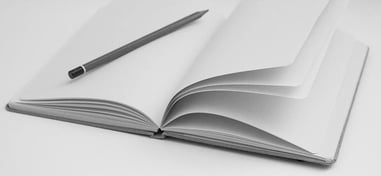 Open notebook with blank pages and a pencil on a table