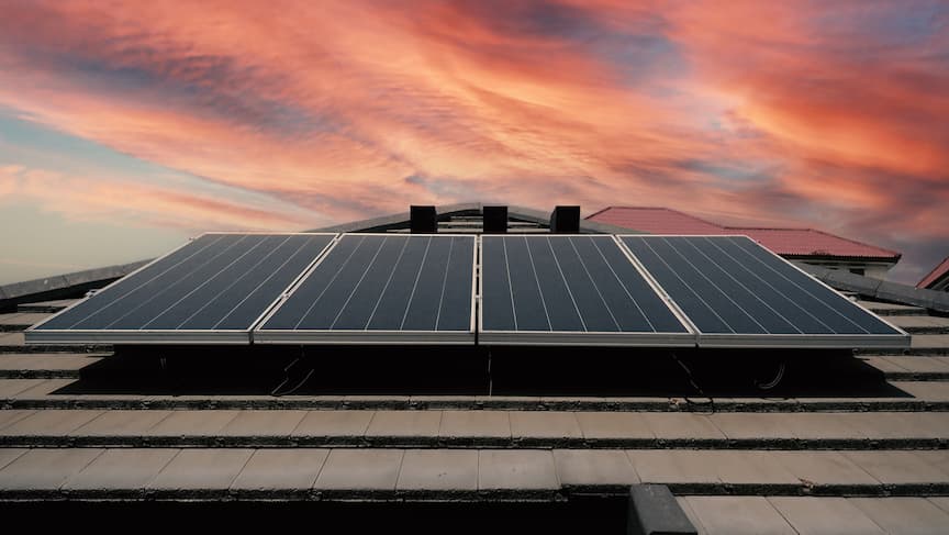 Paneles solares instalados en un tejado con un atardecer de fondo
