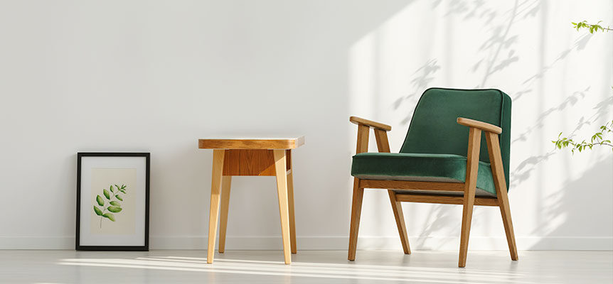 Silla verde con estructura de madera junto a una mesa pequeña y un cuadro apoyado en la pared