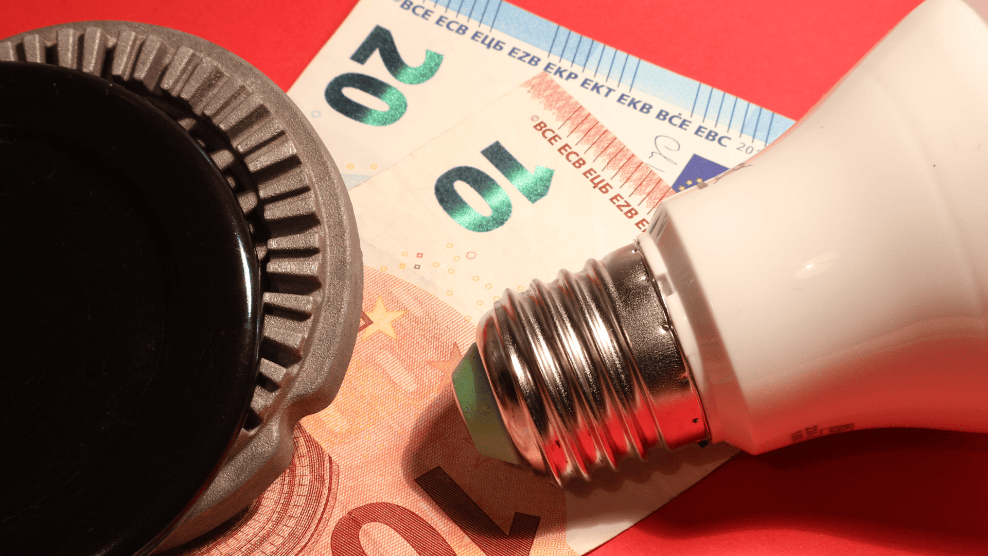 Bombilla LED junto a billetes de euro y un regulador térmico.