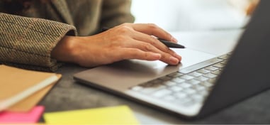 Persona usando un portátil con una mano sobre el touchpad y bolígrafo en la otra
