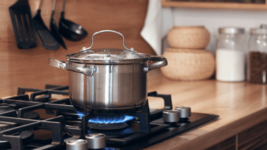 Olla de acero inoxidable calentándose sobre un fogón de gas encendido en una cocina.