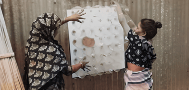 Dos mujeres instalan un panel hecho con botellas de plástico en una pared de chapa