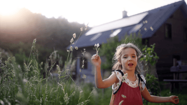 Niña jugando en un entorno natural cerca de una vivienda con paneles solares