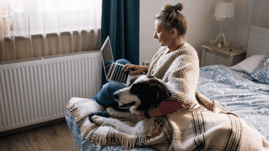 Mujer usando un portátil en casa junto a su perro, en un ambiente doméstico.