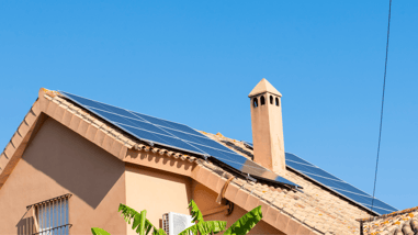 Vivienda con paneles solares instalados en el tejado bajo un cielo azul.