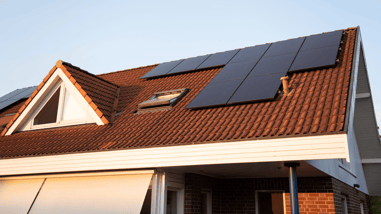 Tejado de vivienda unifamiliar con paneles solares instalados sobre tejas rojas, iluminado por la luz del atardecer.