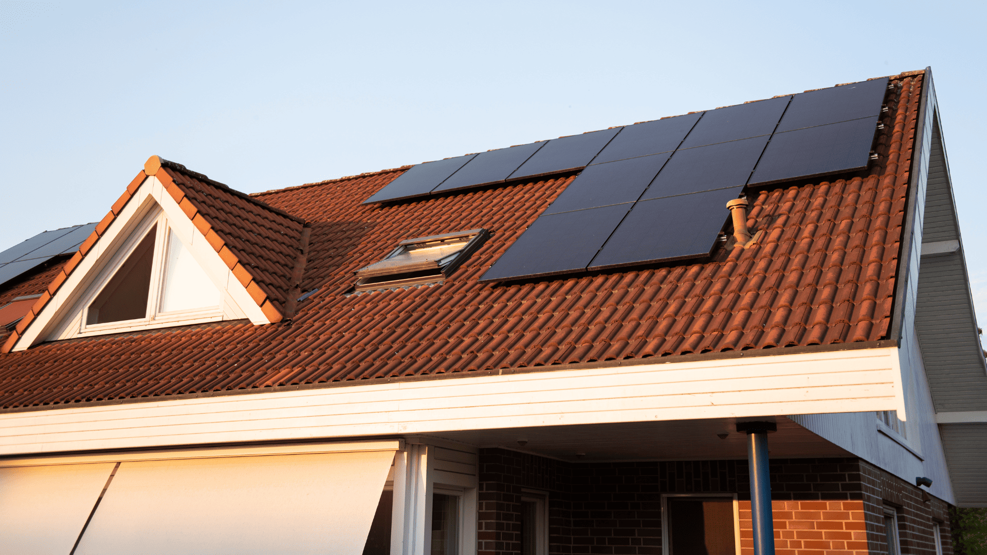 Tejado de vivienda unifamiliar con paneles solares instalados sobre tejas rojas, iluminado por la luz del atardecer.