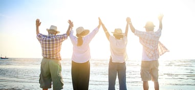 Grupo de personas mayores disfrutando de un día soleado en la playa con los brazos en alto