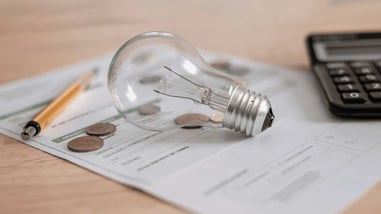 Bombilla sobre una factura de electricidad con monedas, bolígrafo y calculadora, simbolizando el análisis del consumo energético.