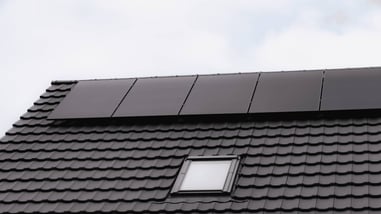 Paneles solares negros instalados sobre un tejado oscuro con ventana.