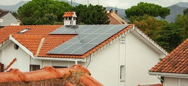 Paneles solares en el tejado de una casa con fondo de montañas y árboles