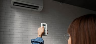 Mujer encendiendo el aire acondicionado con un mando a distancia en casa