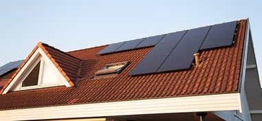 Tejado de una casa con tejas rojas y paneles solares negros instalados