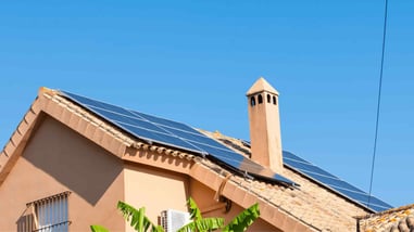 Vivienda con paneles solares instalados en el tejado bajo un cielo azul.