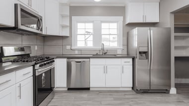 Cocina moderna con electrodomésticos de acero inoxidable, incluyendo frigorífico, lavavajillas, horno y microondas, todo en un entorno de diseño limpio y minimalista.