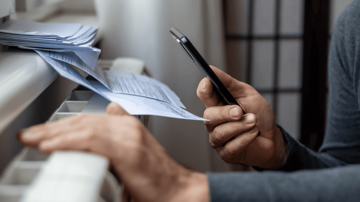 Persona consultando documentos impresos mientras utiliza un teléfono móvil.