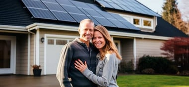 Pareja sonriente frente a su casa con instalación de paneles solares en el tejado.