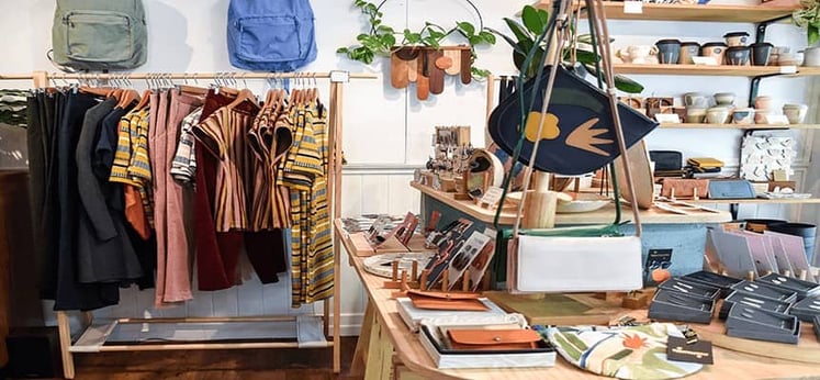 Tienda con ropa colgada, mochilas y accesorios sobre mesas de madera