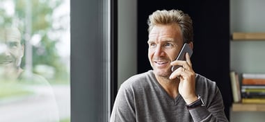 Hombre hablando por teléfono junto a una ventana, con reflejo en el cristal
